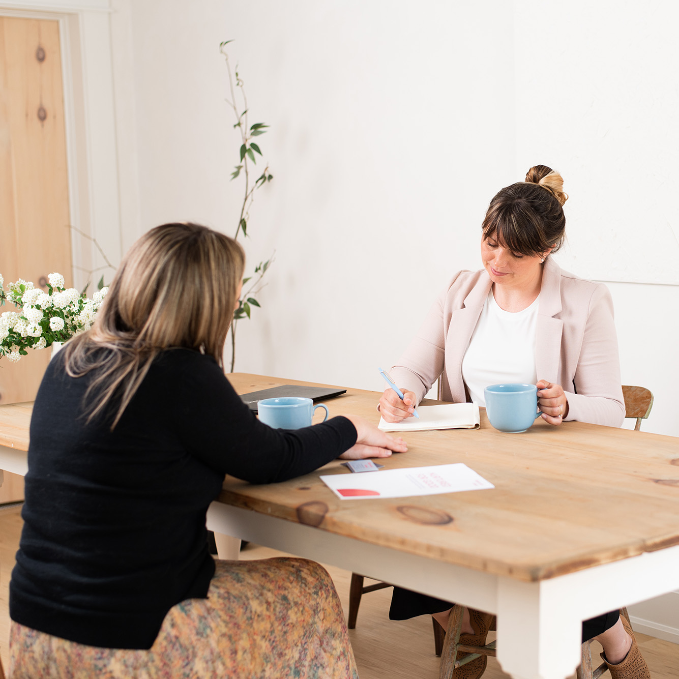 Women sitting at table with blue coffee cups reviewing paperwork