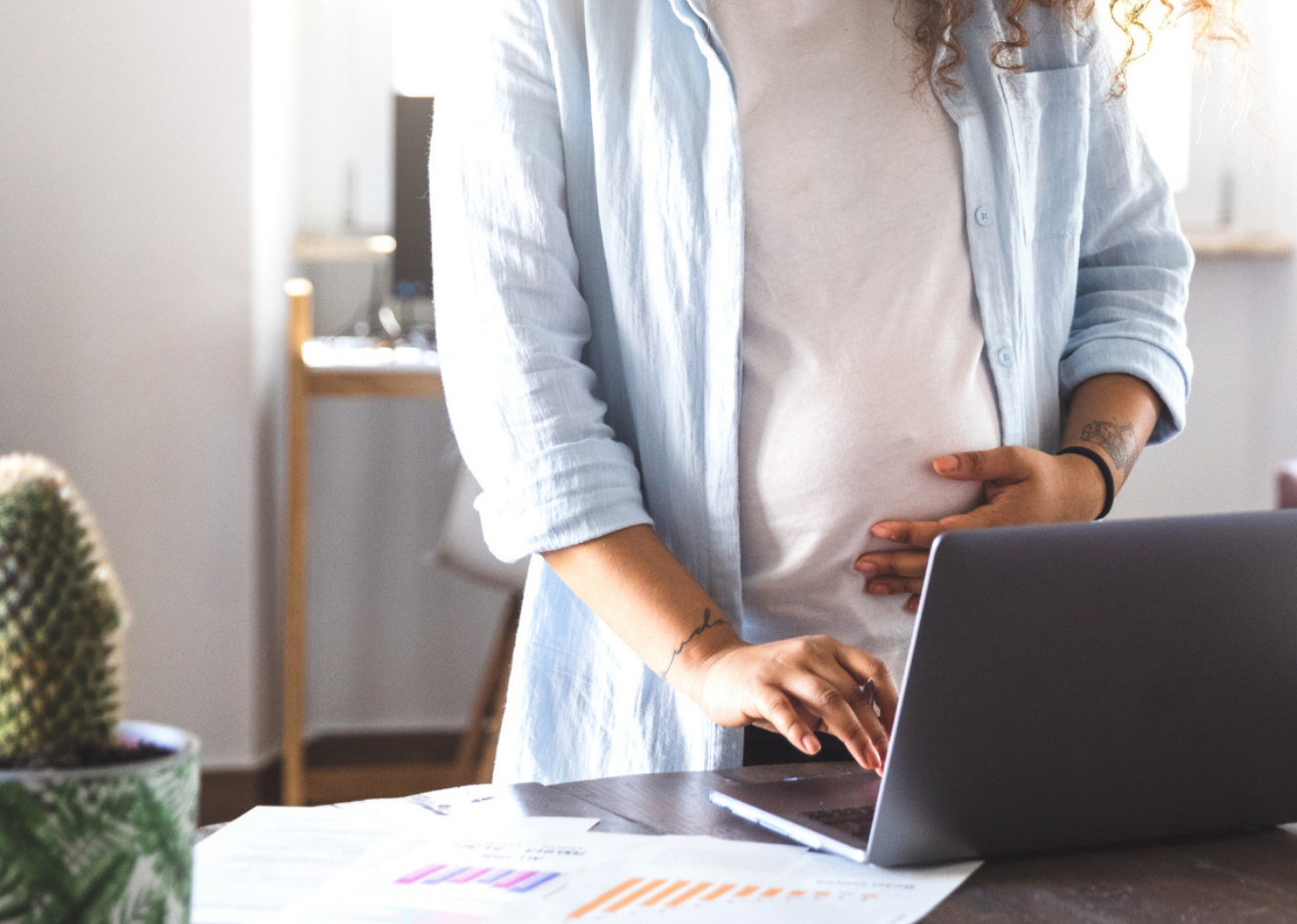 Pregnant person in blue and white standing at laptop