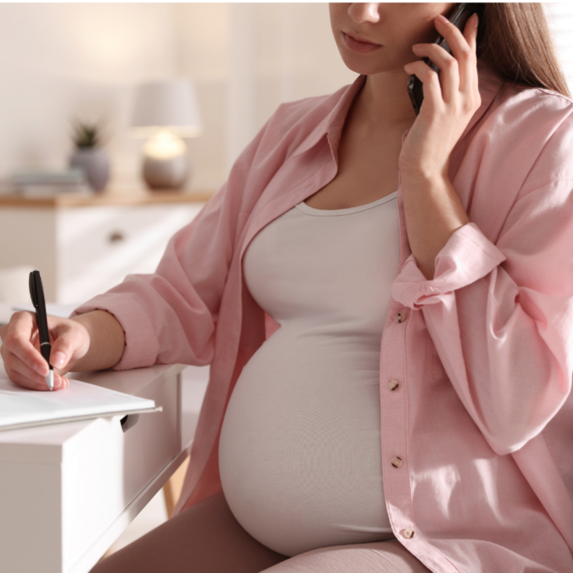 Pregnant person wearing pink and white on phone at desk